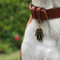 Pet ID tag hanging on a collar worn by a brown and white dog. It is made of gold plated brass and black enamel in the shape of a hamsa.
